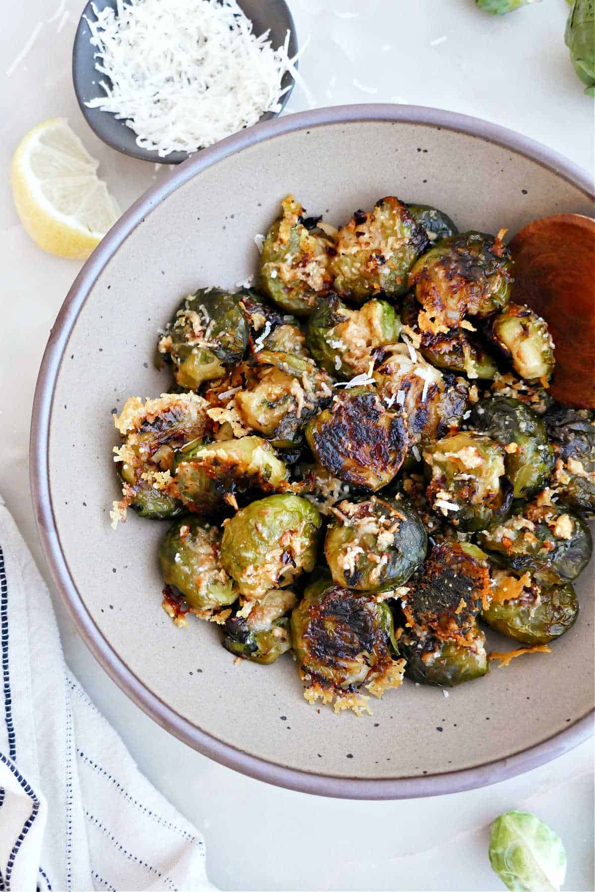 Crispy Brussels sprouts in a bowl next to parmesan cheese, lemon, and a napkin.