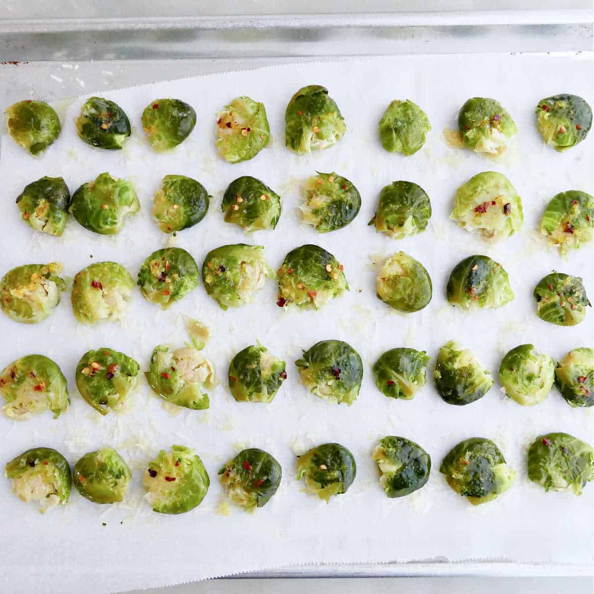 Brussels sprouts smashed and brushed with olive oil and seasonings on a baking sheet.