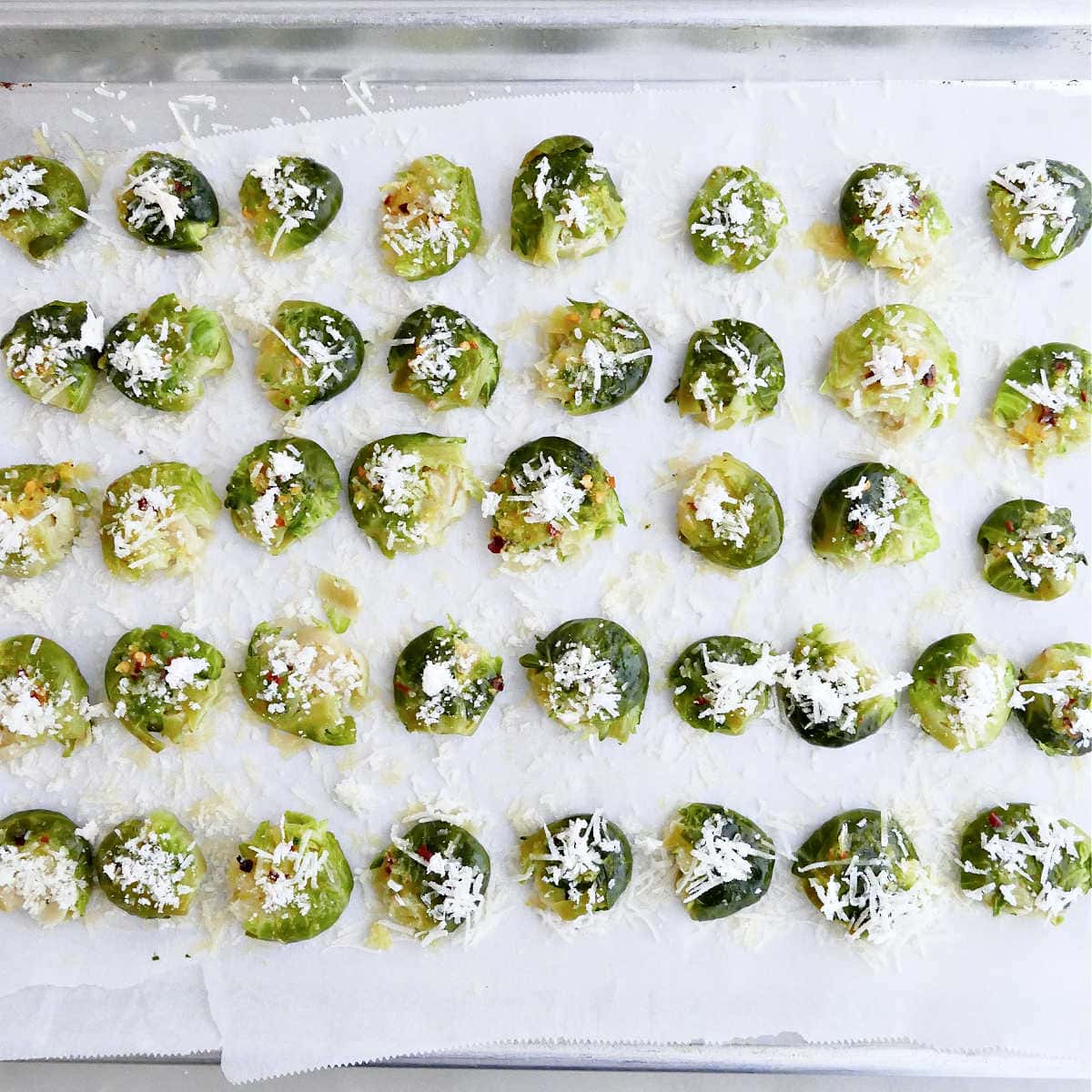 Brussels sprouts sprinkled with parmesan cheese on a sheet pan before being roasted.