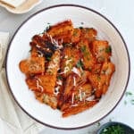 Parmesan smashed carrots in a bowl next to parsley, cheese, and a napkin.
