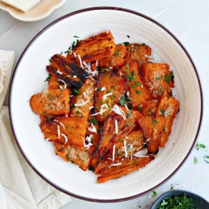 Parmesan smashed carrots in a bowl next to parsley, cheese, and a napkin.