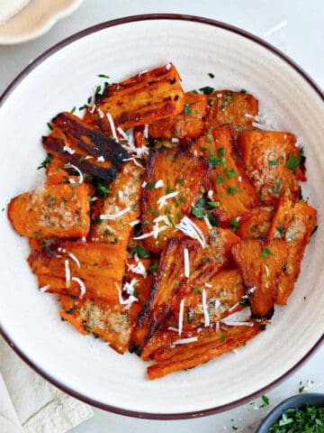 Parmesan smashed carrots in a bowl next to parsley, cheese, and a napkin.