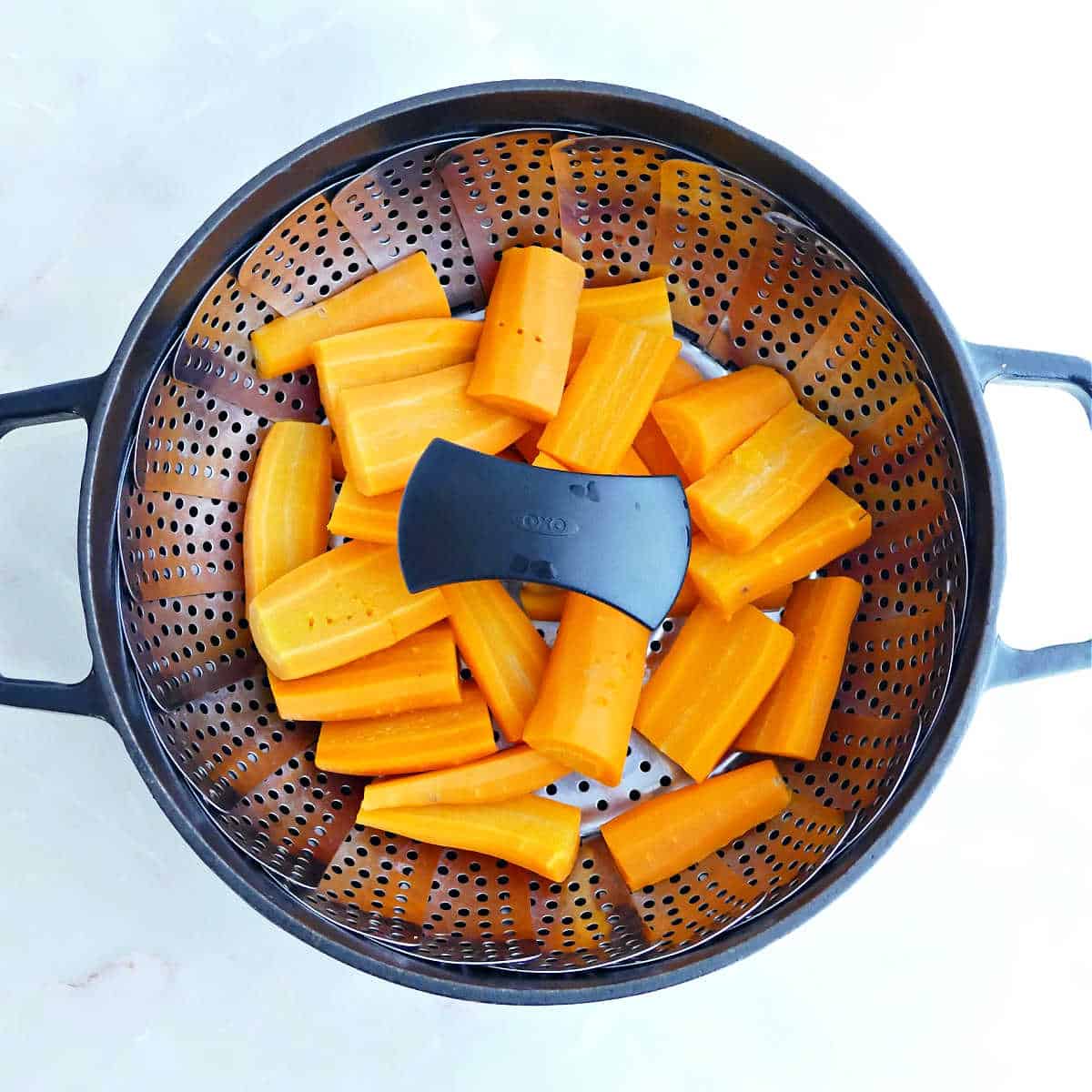 Carrots in a vegetable steamer basket in a pot.