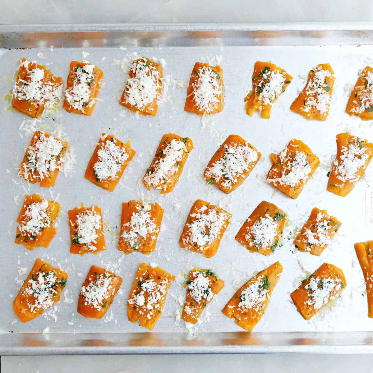 Smashed carrots sprinkled with cheese on a baking sheet before roasting.