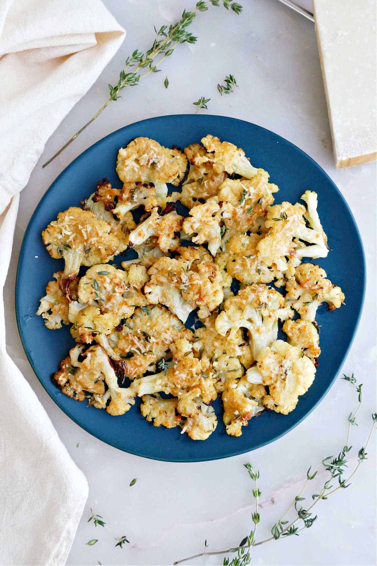 Smashed cauliflower bites on a serving plate next to a napkin and thyme sprigs.