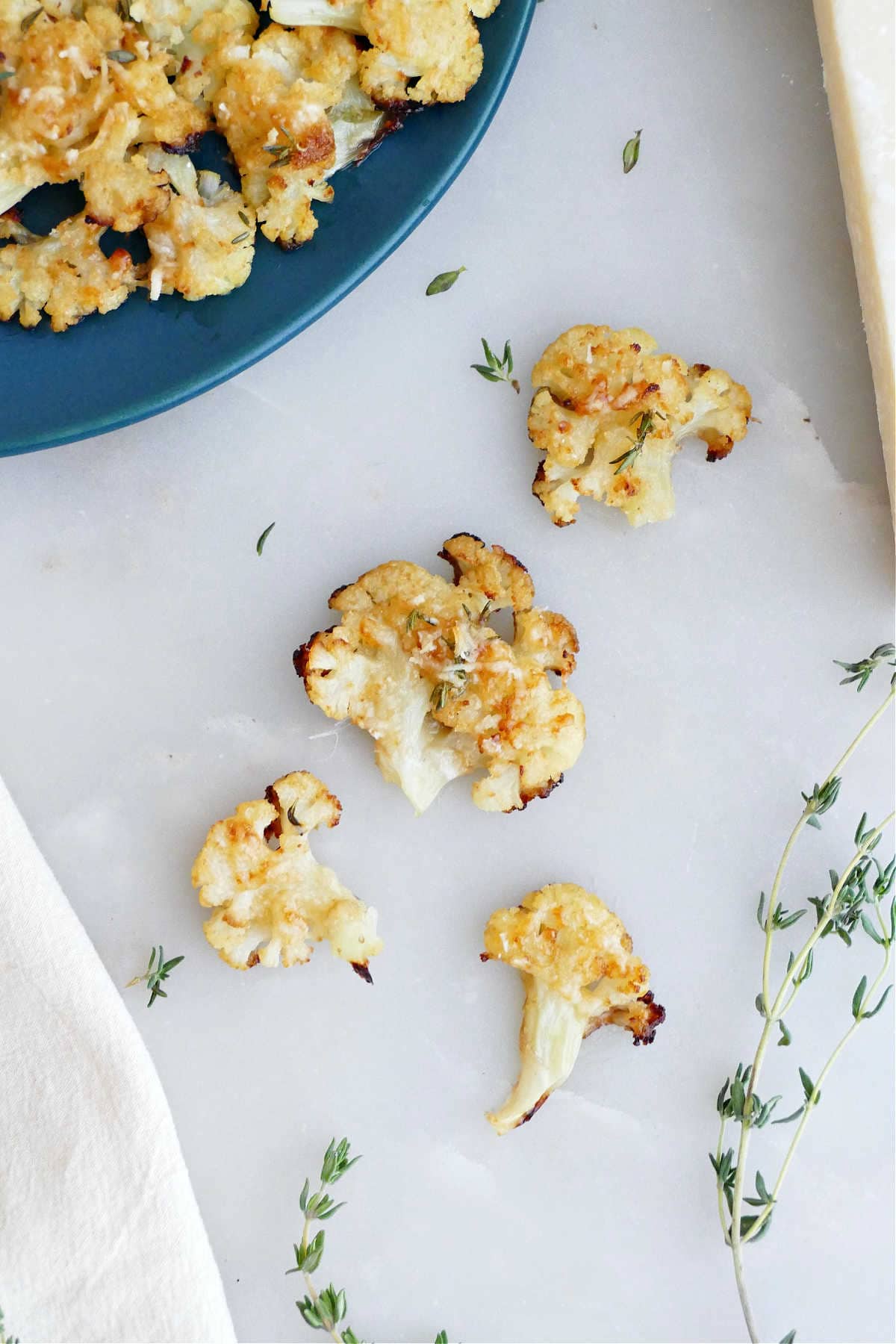 Four smashed cauliflower florets next to a serving plate on a counter.