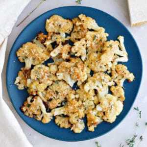 Smashed cauliflower bites on a serving plate next to a napkin and thyme sprigs.
