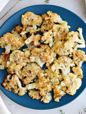 Smashed cauliflower bites on a serving plate next to a napkin and thyme sprigs.