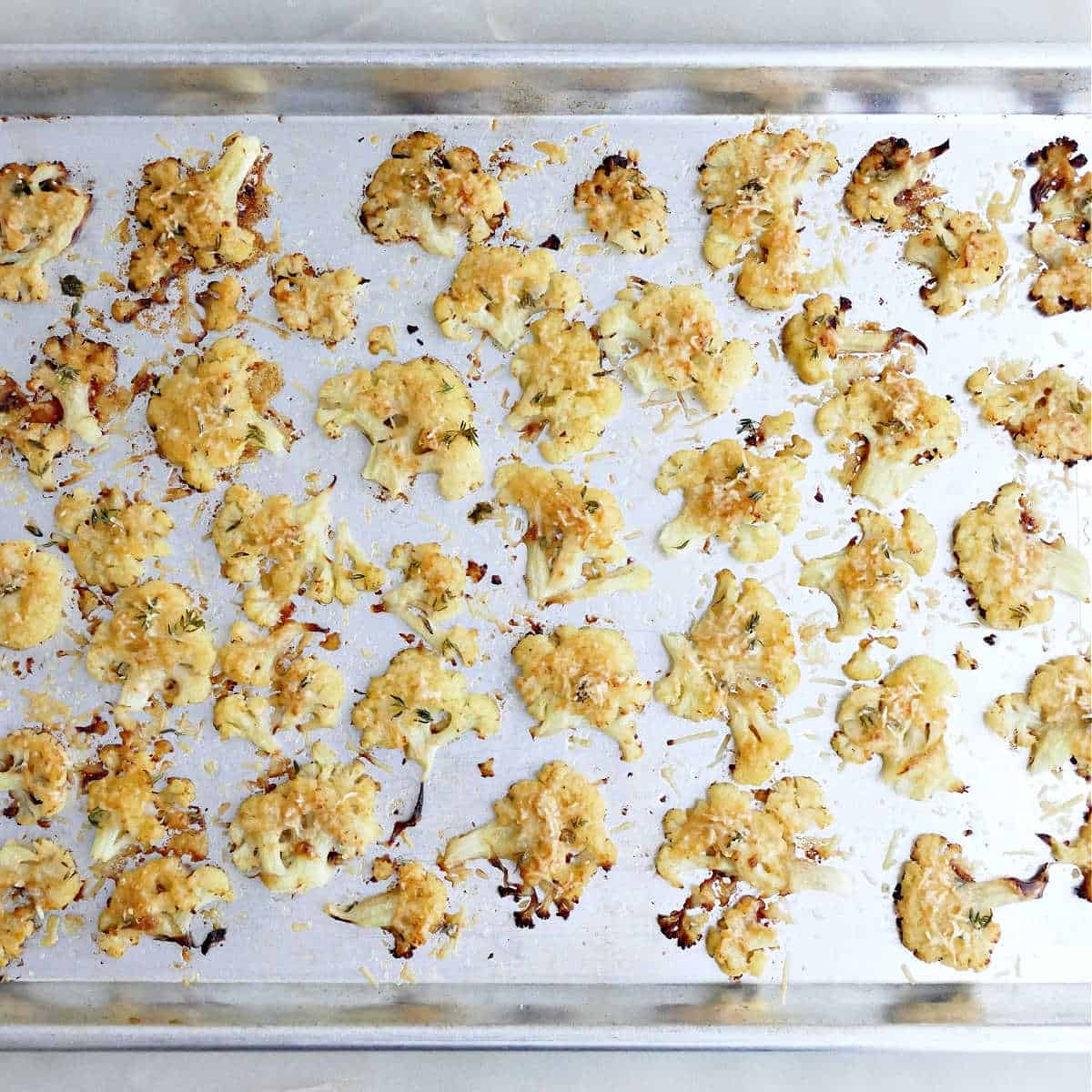 Roasted cauliflower with a cheesy crust on a baking sheet.