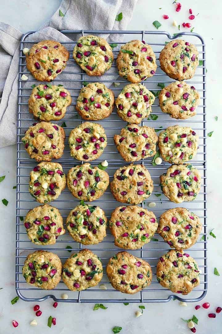 An overhead view of 24 white chocolate chip spinach cookies lined up on a metal cooling rack. 