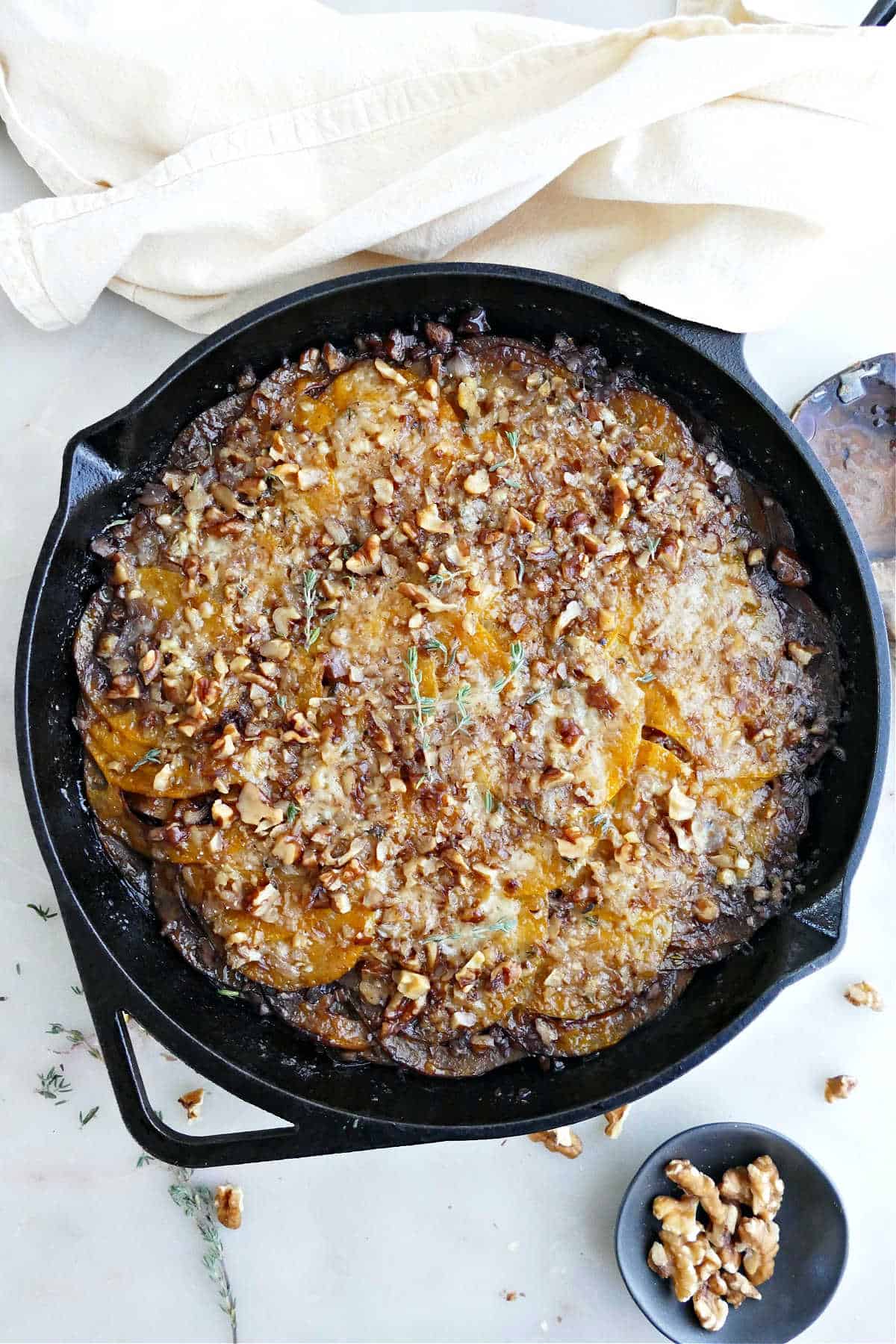Butternut squash gratin in a cast iron skillet next to a napkin and walnuts.