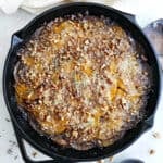 Butternut squash gratin in a cast iron skillet next to a napkin and walnuts.