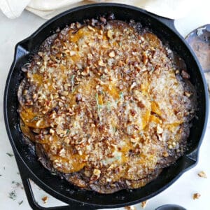 Butternut squash gratin in a cast iron skillet next to a napkin and walnuts.