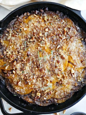 Butternut squash gratin in a cast iron skillet next to a napkin and walnuts.