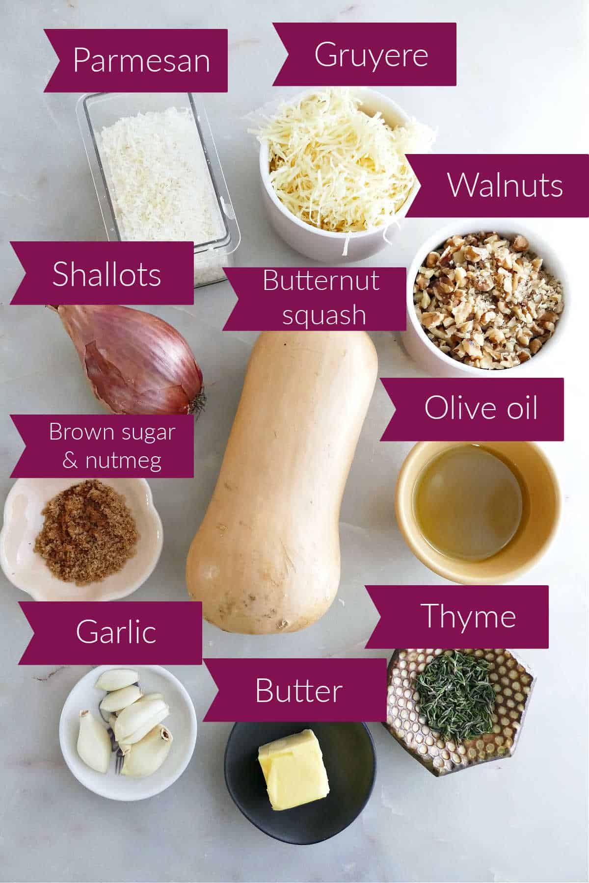 Parmesan, gruyere, walnuts, olive oil, thyme, butter, squash, garlic, brown sugar, and shallots on a counter.