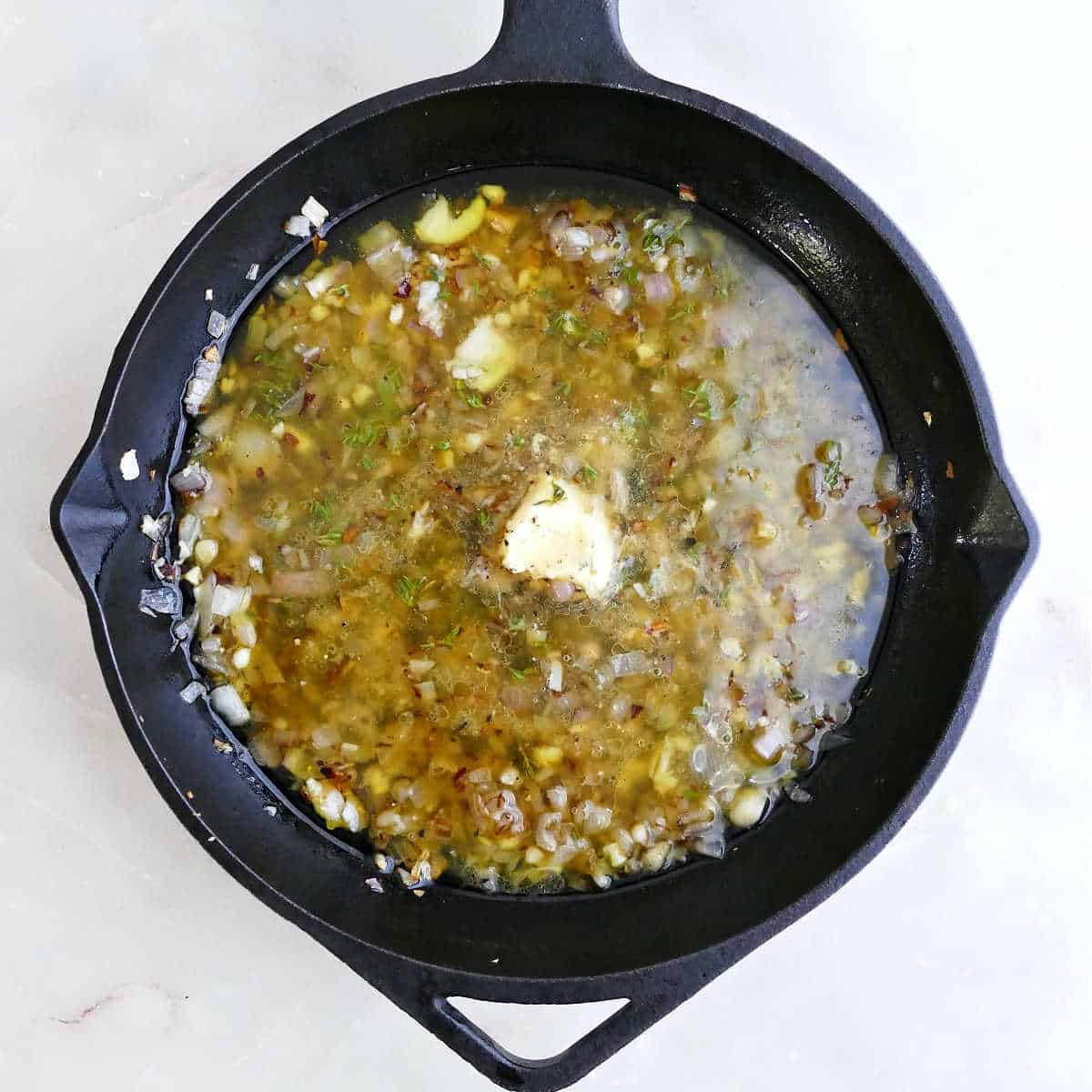 Olive oil, thyme, and butter added to a skillet with onion and garlic.