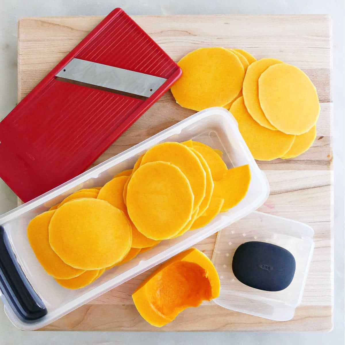 Butternut squash thinly sliced with a mandoline on a cutting board.