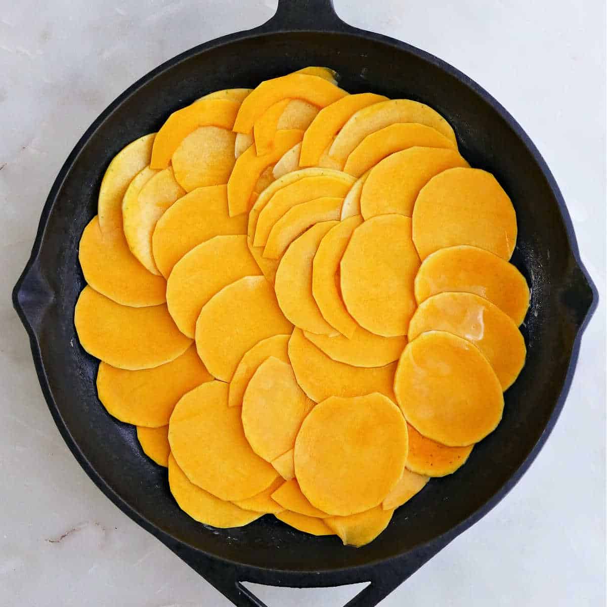 Thin butternut squash slices overlapping in a cast iron skillet.