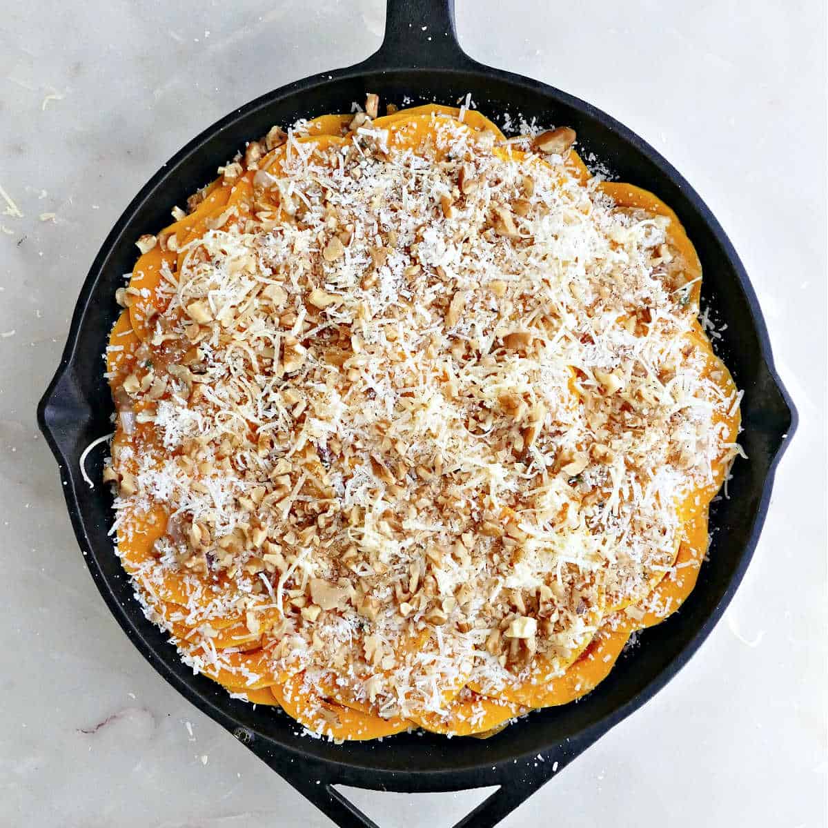 Squash gratin layers topped with cheese and walnuts before baking.