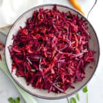 Carrot beet salad in a serving bowl next to ingredients, spoon, and napkin.