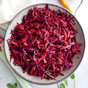 Carrot beet salad in a serving bowl next to ingredients, spoon, and napkin.
