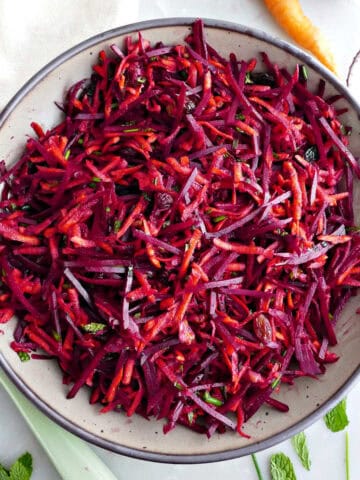 Carrot beet salad in a serving bowl next to ingredients, spoon, and napkin.