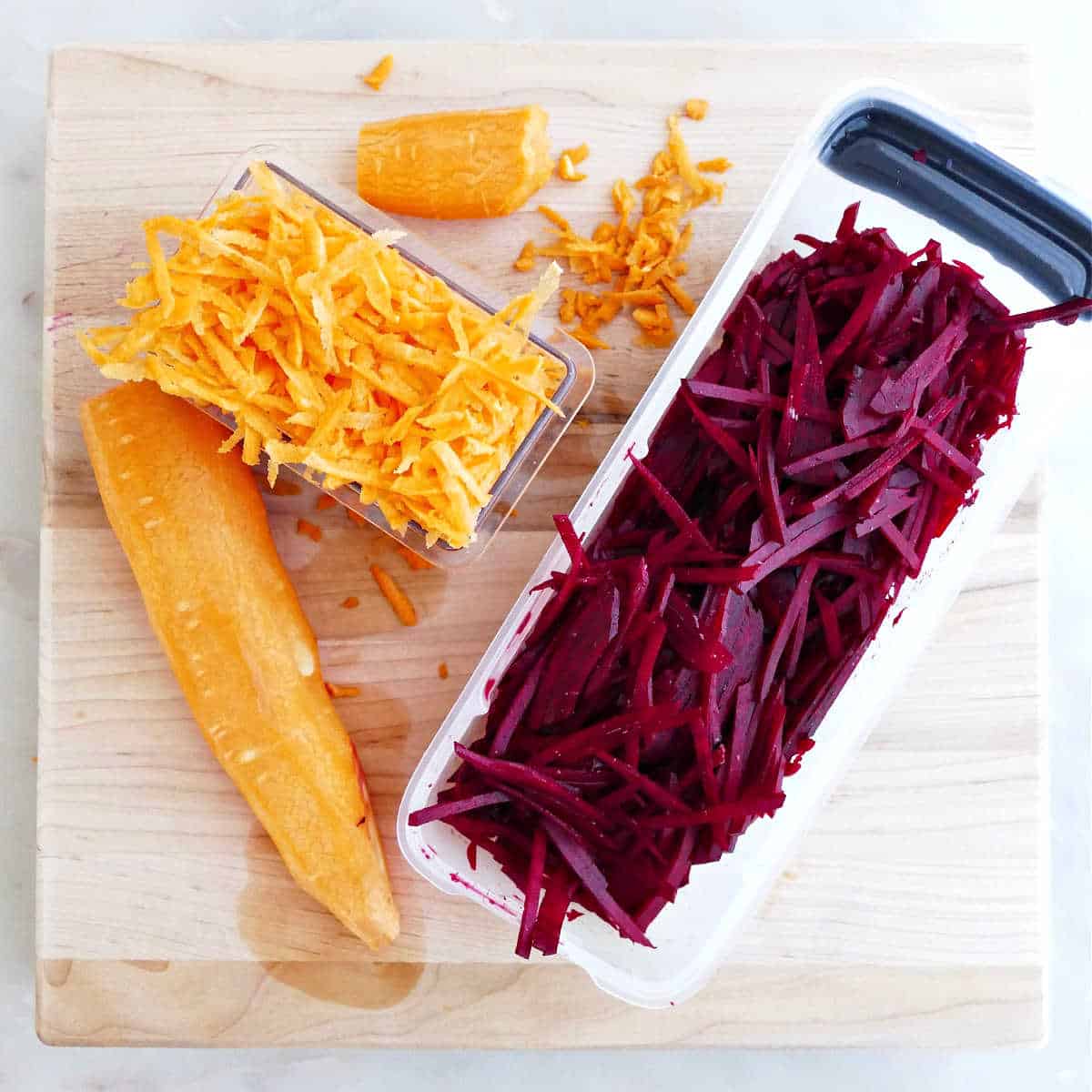 Grated carrots and beets in containers on a cutting board.