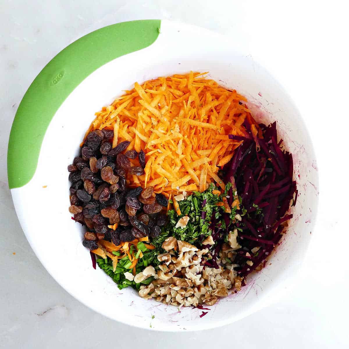 Golden raisins, grated vegetables, chopped walnuts, and herbs in a mixing bowl.