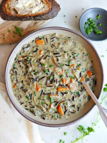 Wild rice soup in a bowl with a spoon next to bread, napkin, and parsley.