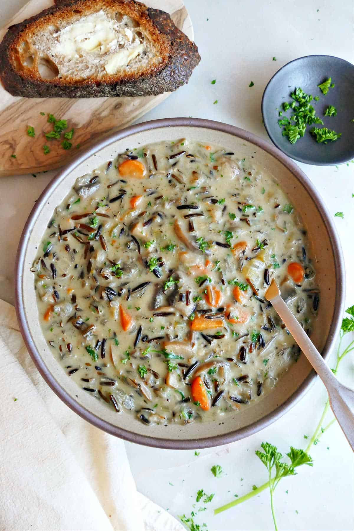 Wild rice soup in a bowl with a spoon next to bread, napkin, and parsley.