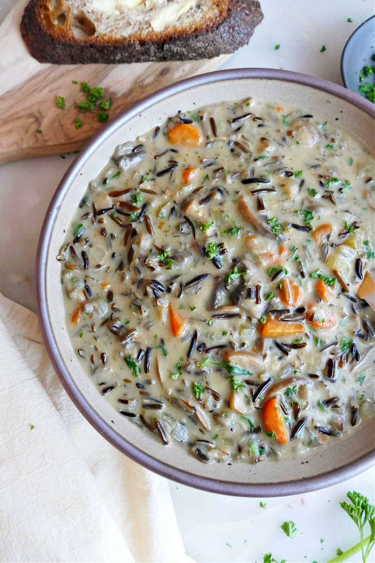 Cream of mushroom wild rice soup in a serving bowl next to bread.