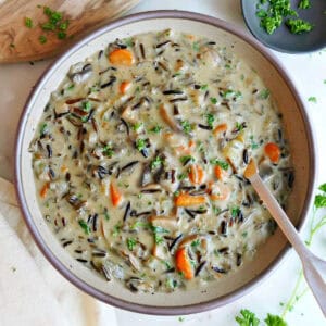 Wild rice soup in a bowl with a spoon next to bread, napkin, and parsley.