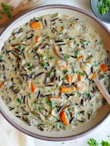 Wild rice soup in a bowl with a spoon next to bread, napkin, and parsley.