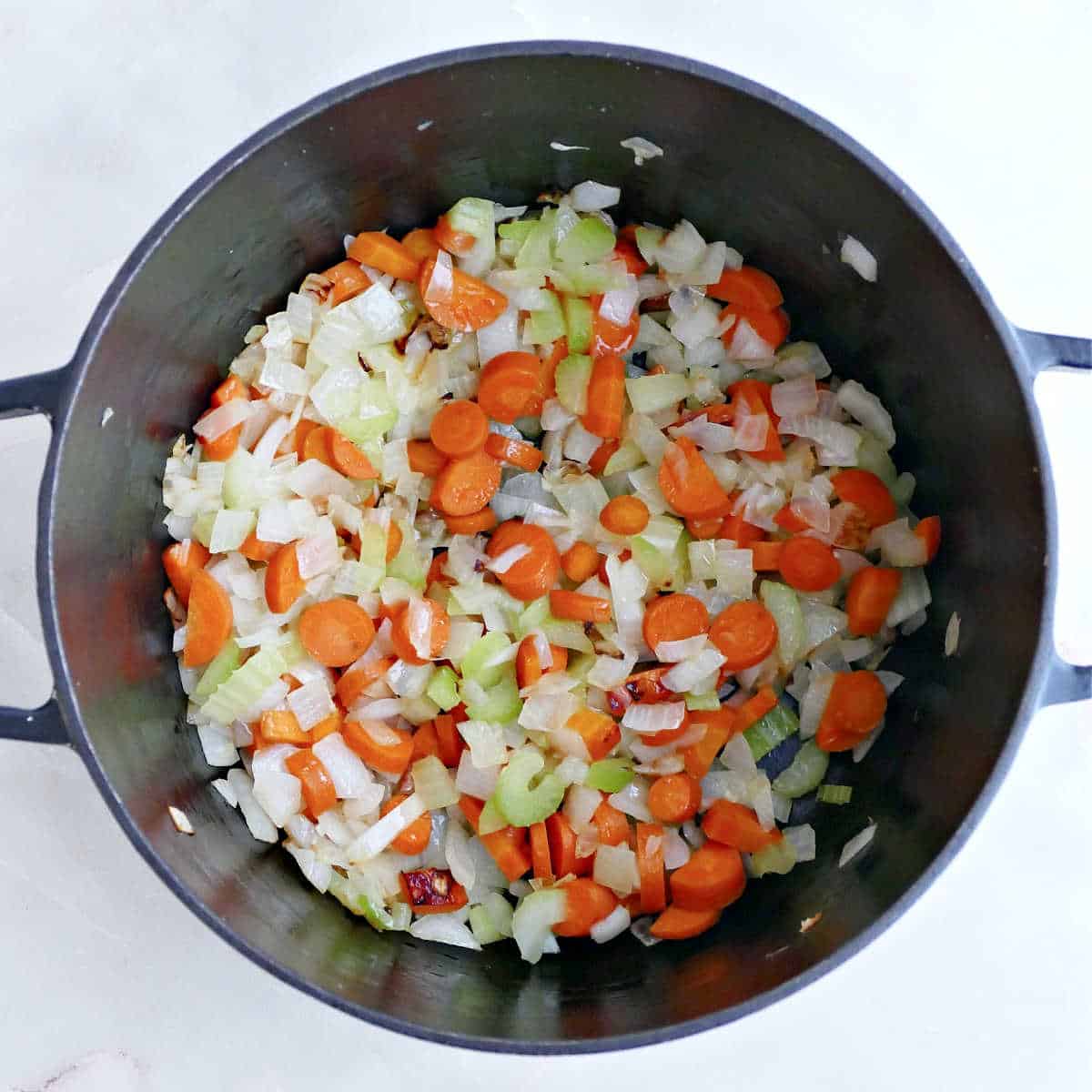Onions, carrot, and celery cooking in a soup pot.