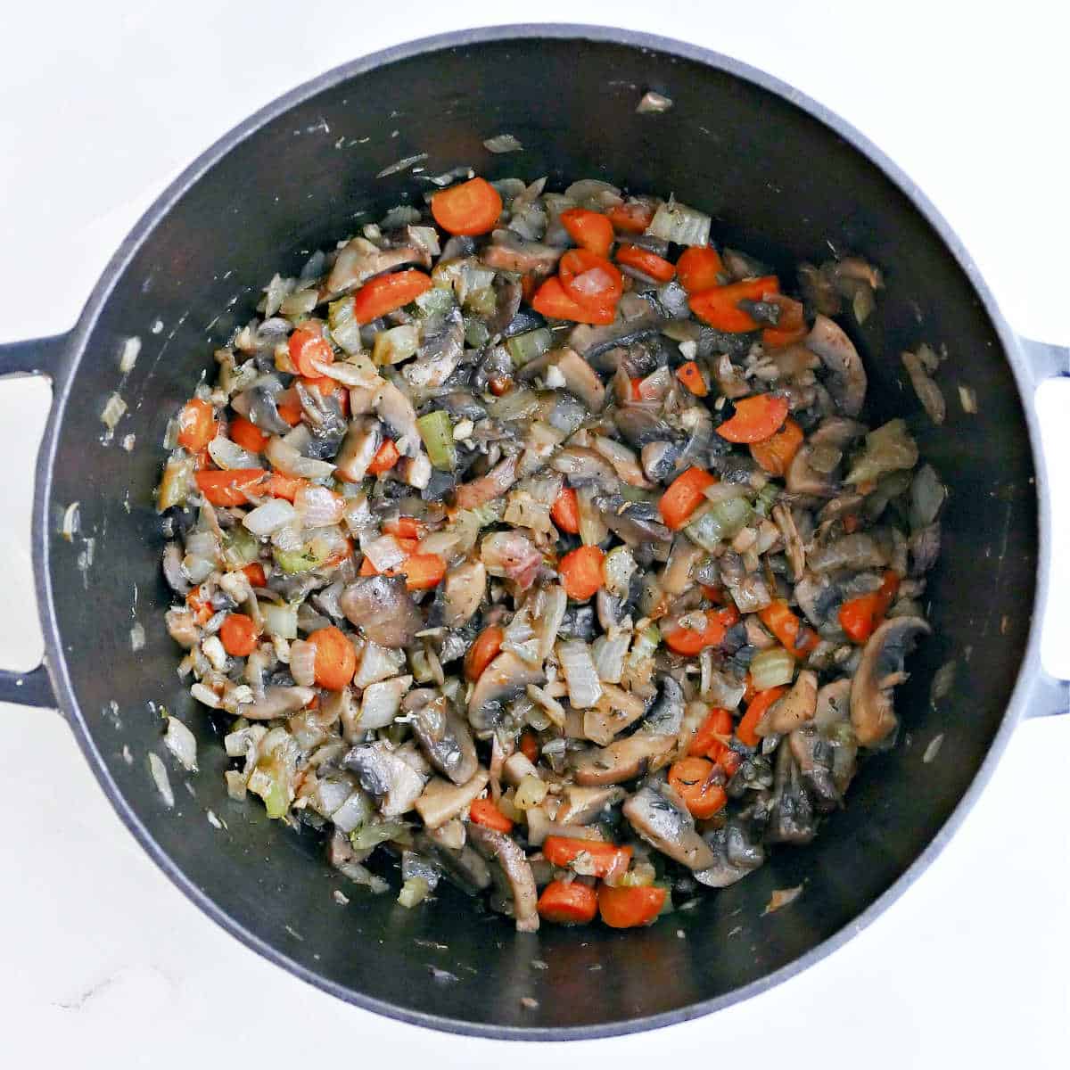 Mushrooms, onions, carrots, celery, garlic, and spices cooking in a soup pot.