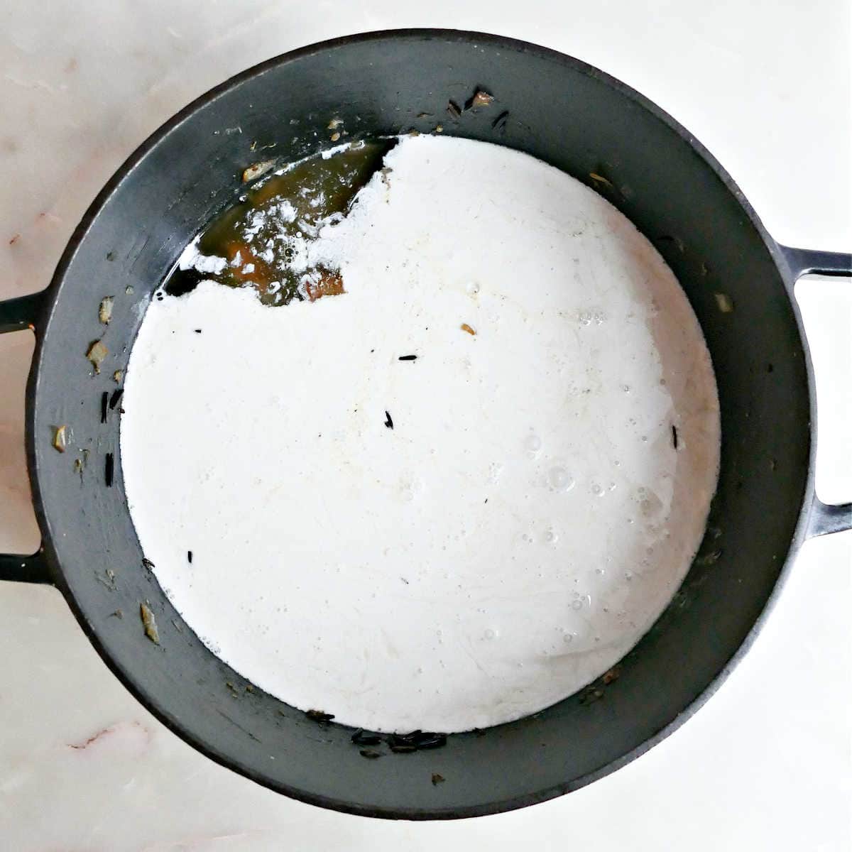 Coconut milk and vegetable broth added to soup ingredients in a pot.