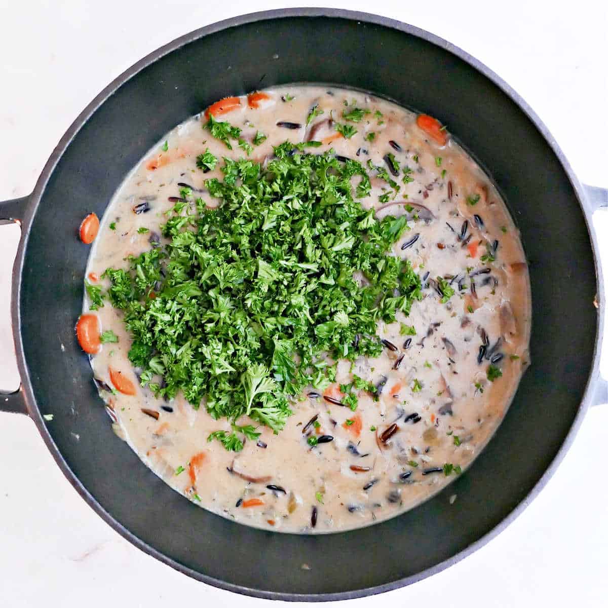 Mushroom and wild rice soup in a pot with chopped parsley being added.