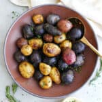 Roasted potatoes in a serving bowl with a spoon next to herbs and a napkin.