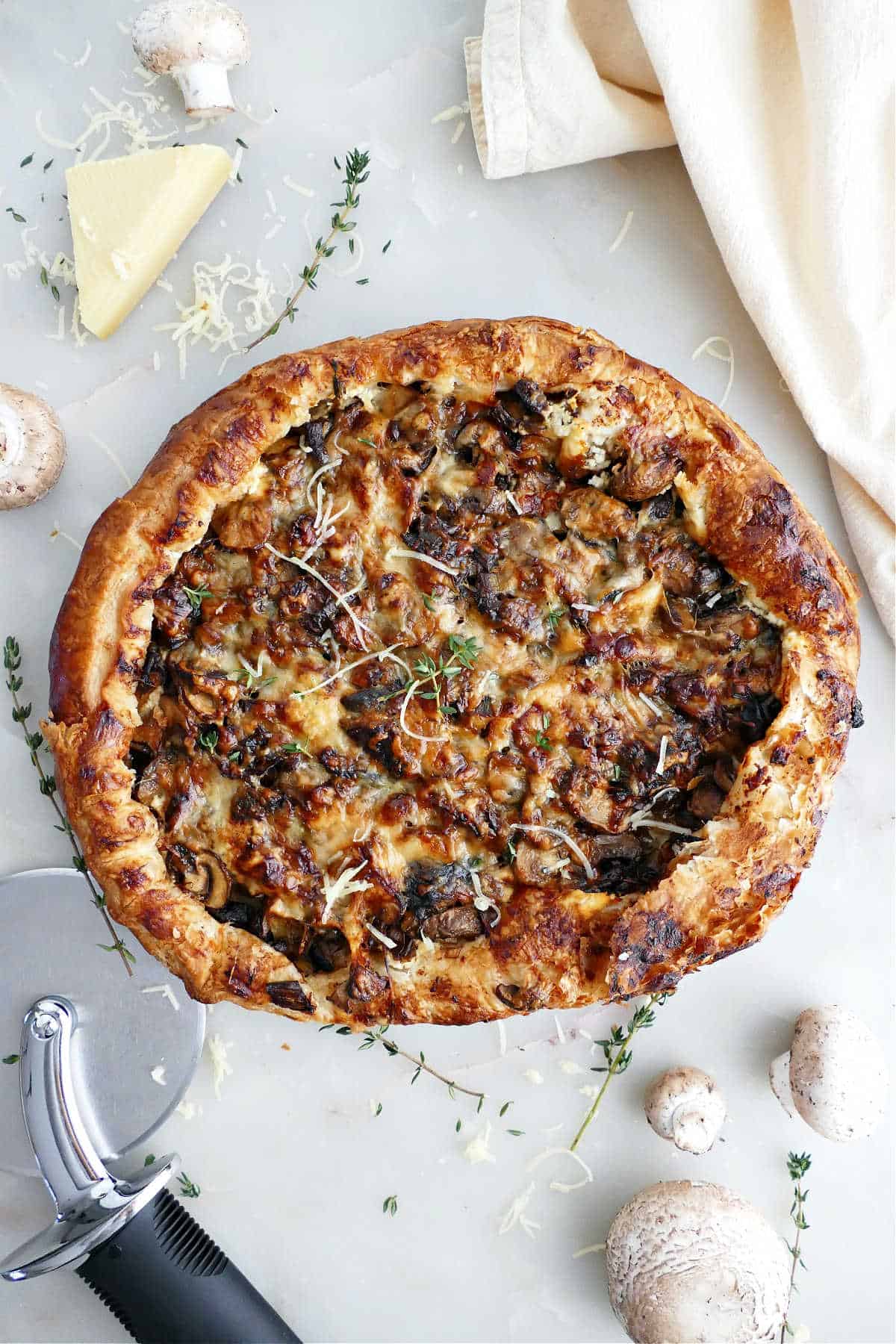 Mushroom galette on a counter next to ingredients, napkin, and pizza cutter.