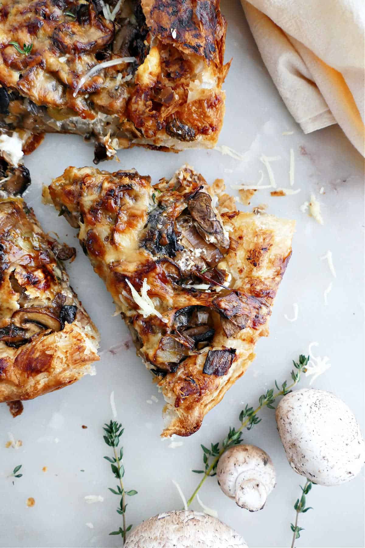 Slice of mushroom galette on puff pastry on a counter next to ingredients.