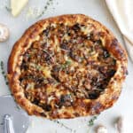 Mushroom galette on a counter next to ingredients, napkin, and pizza cutter.