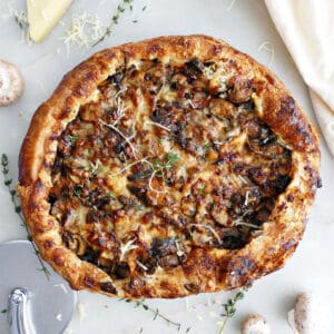 Mushroom galette on a counter next to ingredients, napkin, and pizza cutter.