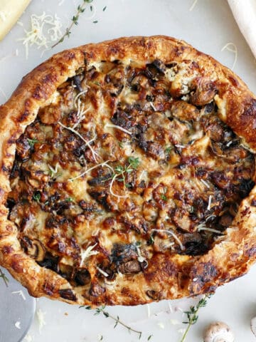 Mushroom galette on a counter next to ingredients, napkin, and pizza cutter.