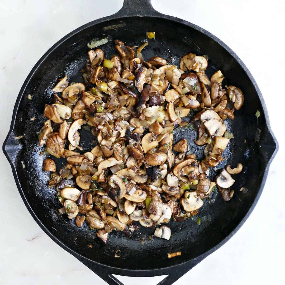 Mushrooms and leeks cooking with balsamic and thyme in a cast iron skillet.