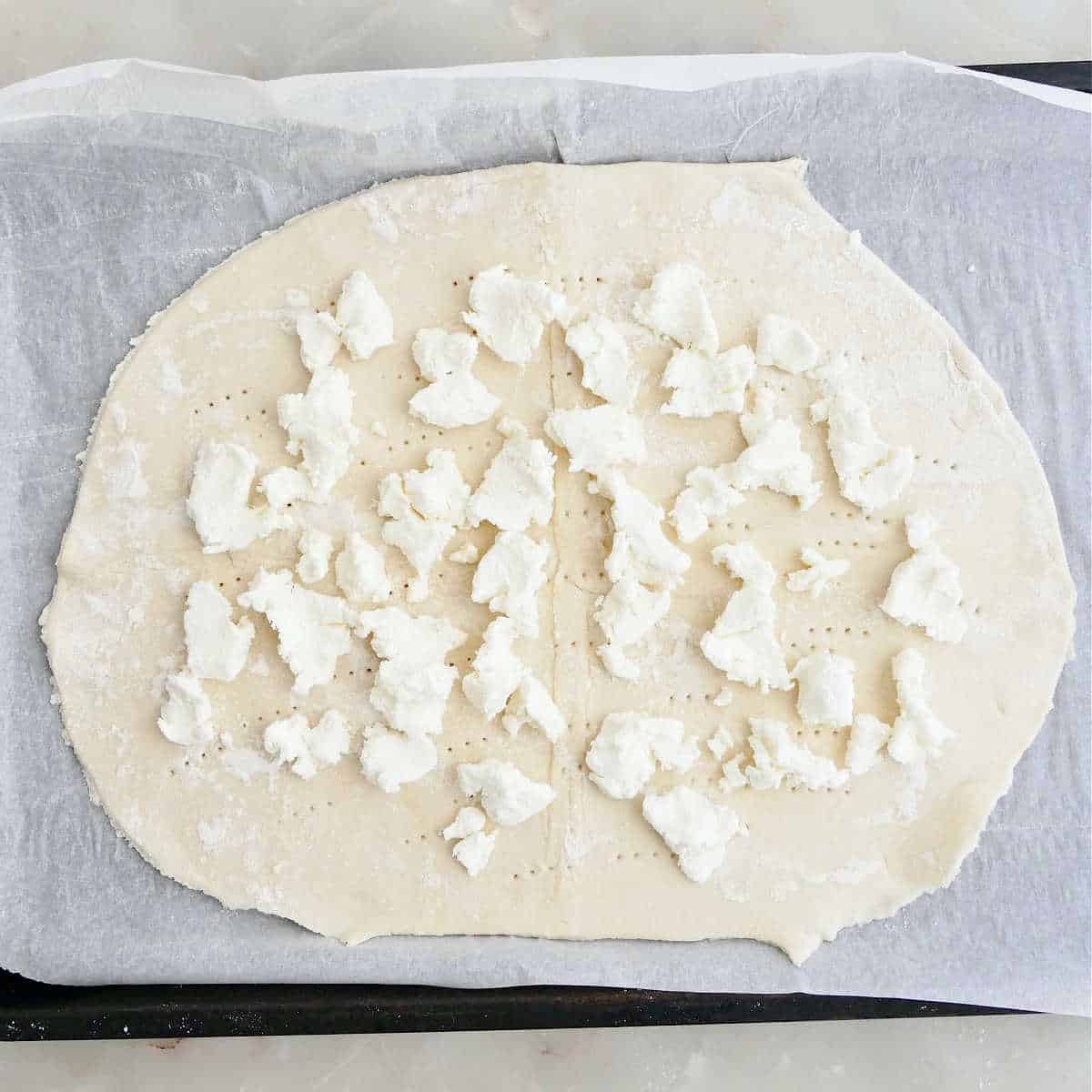 Puff pastry with dollops of goat cheese on top on a baking sheet.