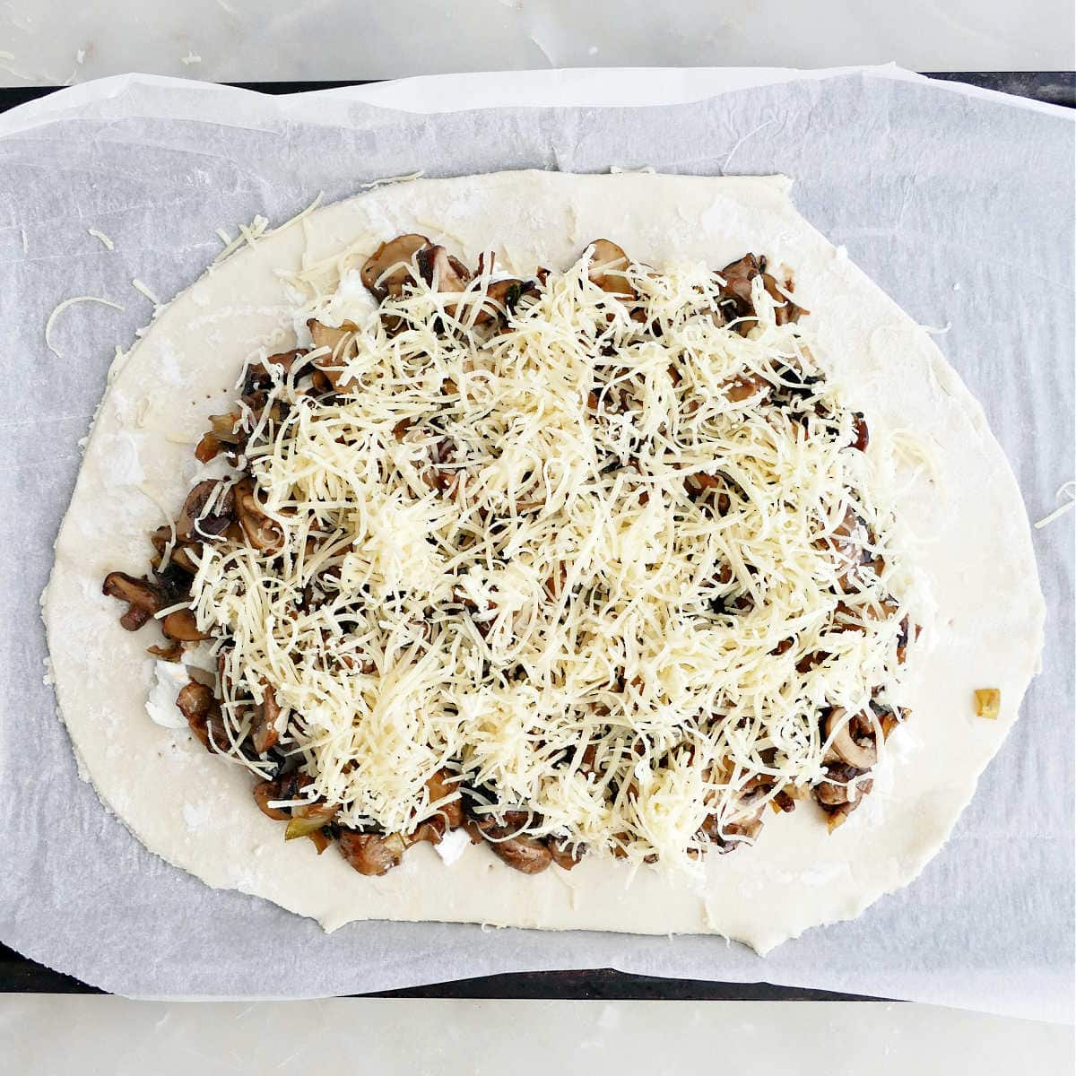 Puff pastry with goat cheese, mushrooms, and shredded cheese on top.
