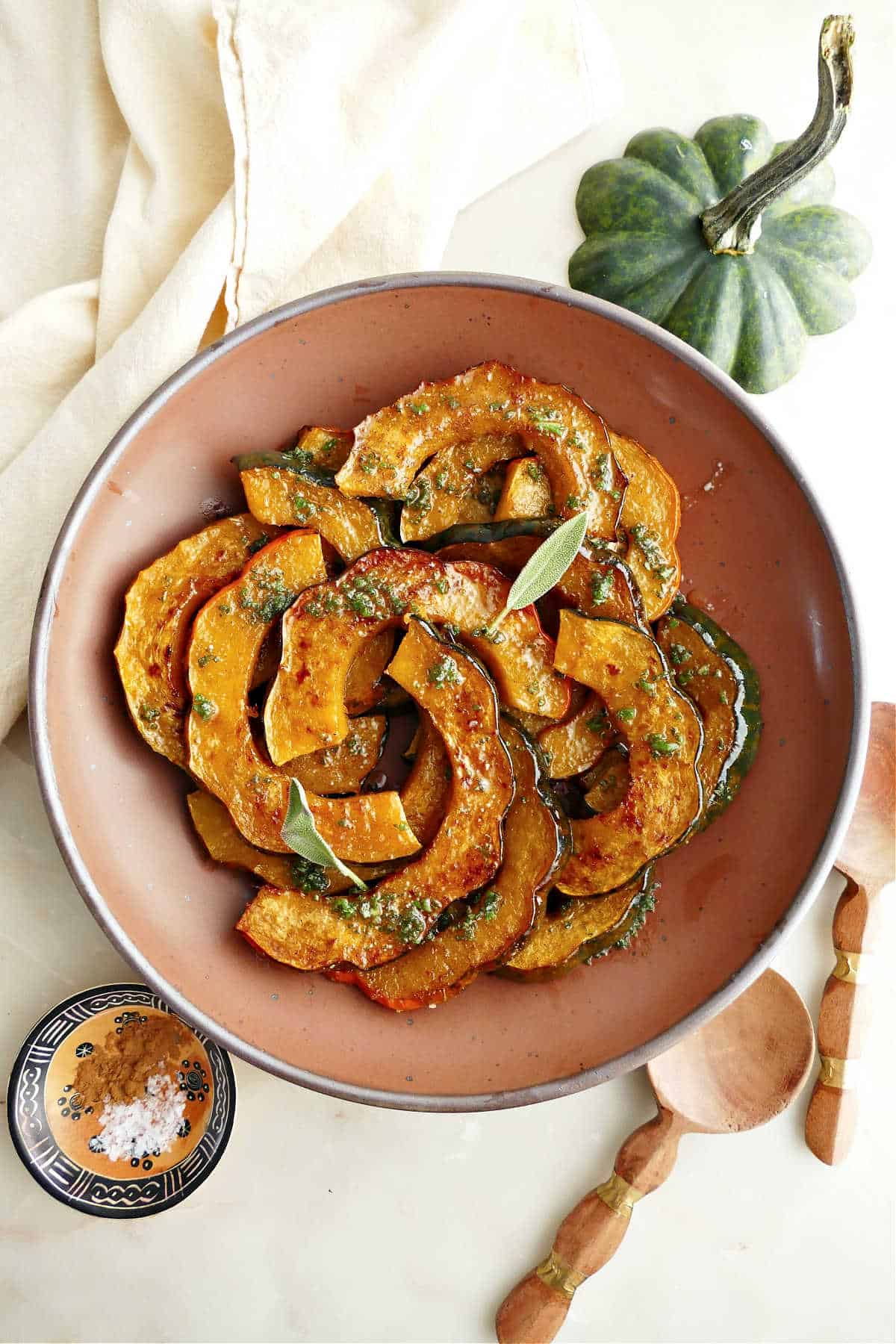 Roasted acorn squash in a serving bowl next to spices, spoons, squash stem, and napkin.