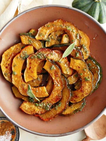 Roasted acorn squash in a serving bowl next to spices, spoons, squash stem, and napkin.