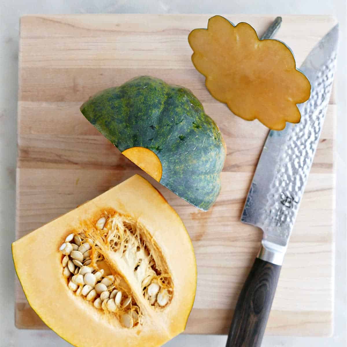 Acorn squash cut in half on a cutting board next to a knife.