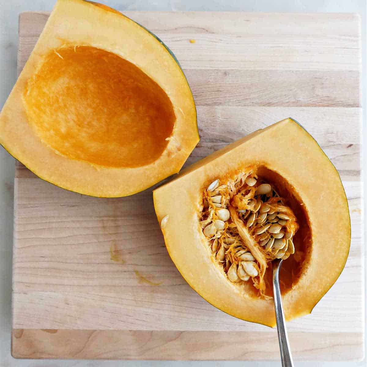 Seeds being scooped out of acorn squash halves on a cutting board.